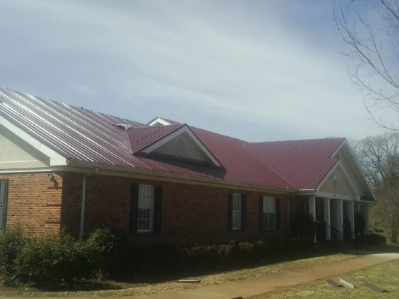 Red metal roof with gabled entries on a long brick building, from a Hail Damage Roof Repair job in Napoleon