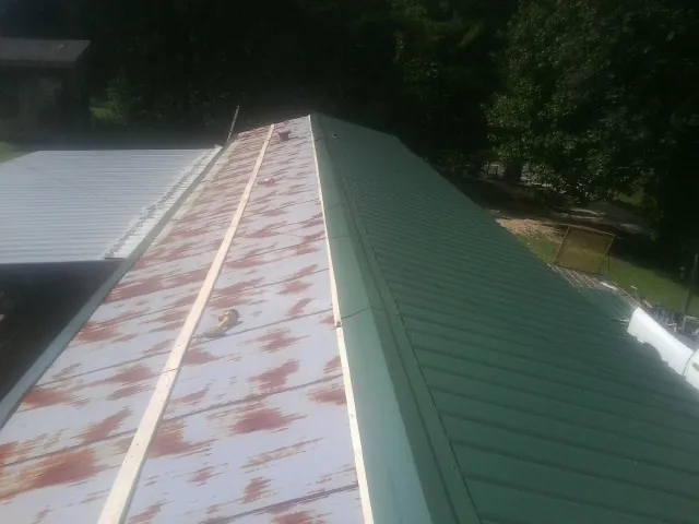 Old rusted panels beside newly installed green metal roofing — Wind Damage Roof Repair by Roofing Brothers in Napoleon