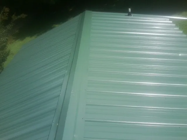 New green metal panels meeting at the ridge of a roof — Flat Roof Repair work by our crew in Napoleon