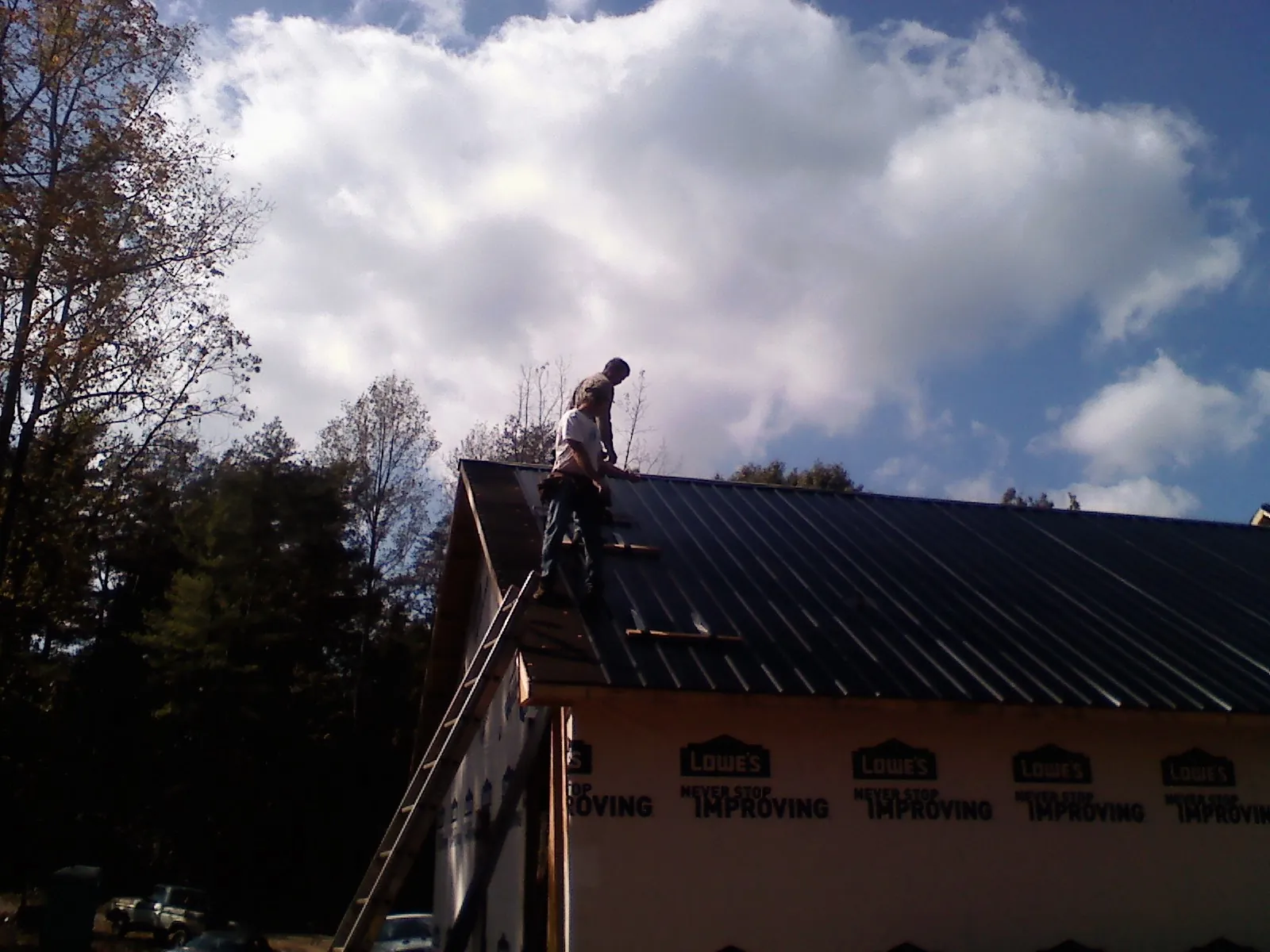 Roofer fastening dark metal panels high against a cloudy sky, from a Roof Inspection job in Napoleon