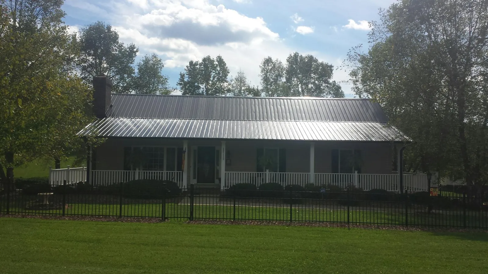 Gray metal roof on a brick ranch with a full width front porch — Gutter Guard Installation work by our crew in Napoleon